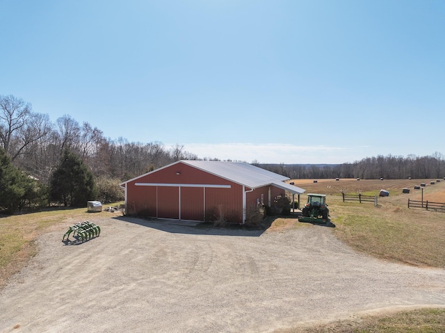 view of pole building featuring driveway, a rural view, fence, and a yard