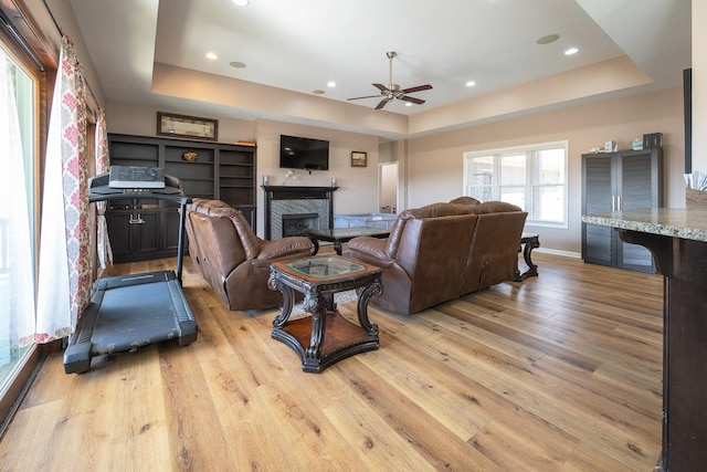 living area with light wood-style floors, a raised ceiling, and a glass covered fireplace