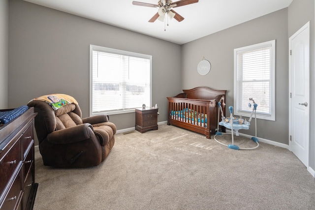 bedroom featuring baseboards, a crib, a ceiling fan, and light colored carpet