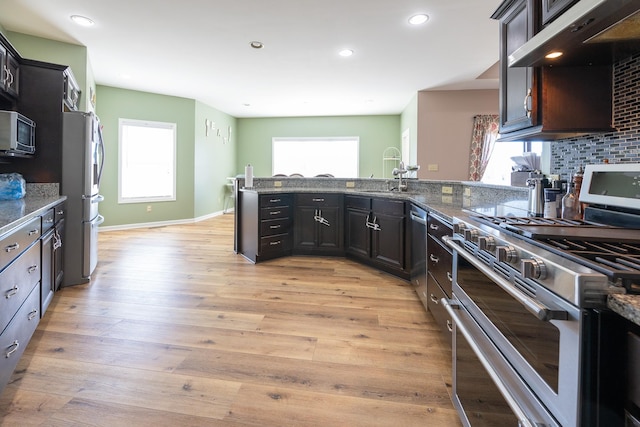 kitchen with under cabinet range hood, stainless steel appliances, a sink, light wood-style floors, and tasteful backsplash