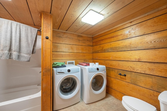 washroom with light tile patterned floors, wooden ceiling, wood walls, washer and dryer, and laundry area