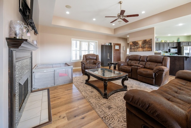 living area featuring a tray ceiling, a fireplace, light wood-style flooring, and recessed lighting