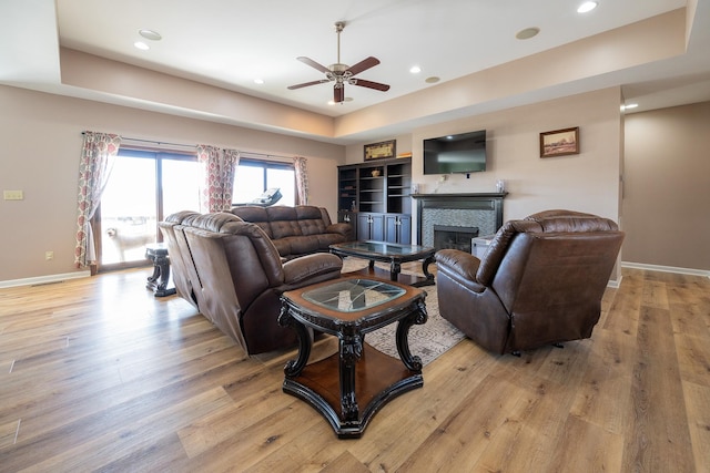 living room with a tray ceiling, baseboards, a fireplace, and light wood finished floors