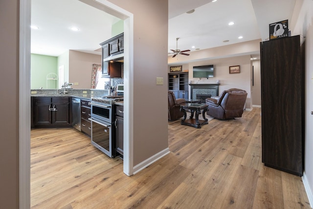 kitchen with light wood finished floors, ceiling fan, appliances with stainless steel finishes, open floor plan, and a fireplace