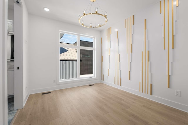 spare room featuring an inviting chandelier, baseboards, visible vents, and wood finished floors