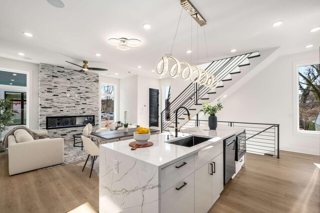 kitchen with a tile fireplace, light wood-style flooring, a sink, open floor plan, and dishwasher