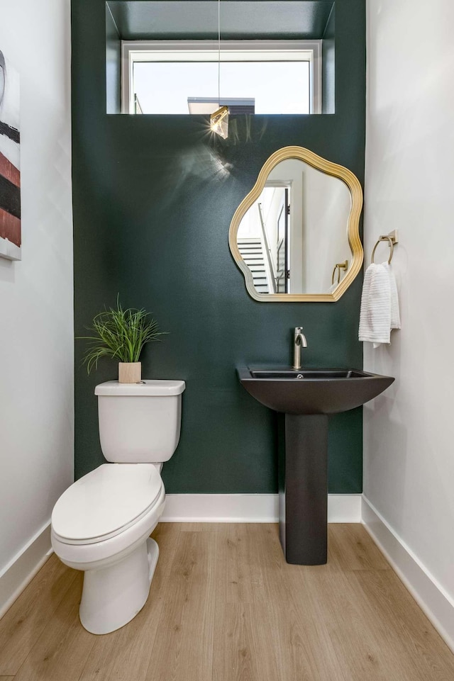 half bath with baseboards, toilet, and wood finished floors