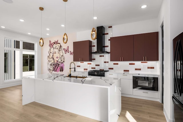 kitchen with a sink, light wood-style floors, wall chimney range hood, black appliances, and modern cabinets