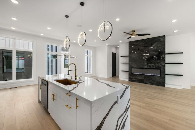 kitchen with dishwasher, an island with sink, light wood-style flooring, a sink, and a high end fireplace