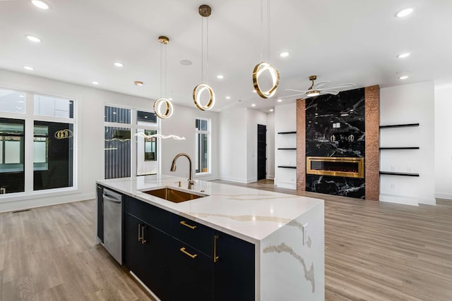 kitchen with open floor plan, a sink, dark cabinetry, stainless steel dishwasher, and a high end fireplace