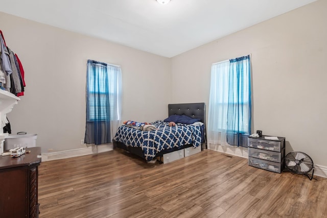 bedroom with multiple windows, wood finished floors, and baseboards