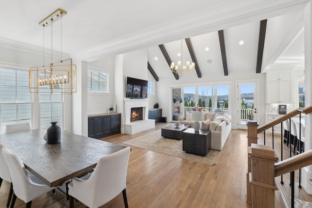 living room featuring beam ceiling, a notable chandelier, stairway, light wood-type flooring, and a warm lit fireplace