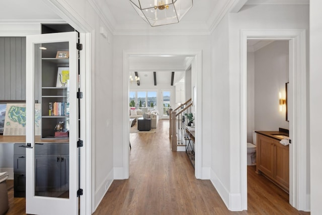 corridor with baseboards, wood finished floors, an inviting chandelier, stairs, and crown molding