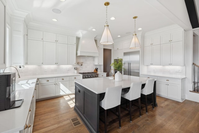 kitchen with built in fridge, light countertops, custom range hood, and wood finished floors