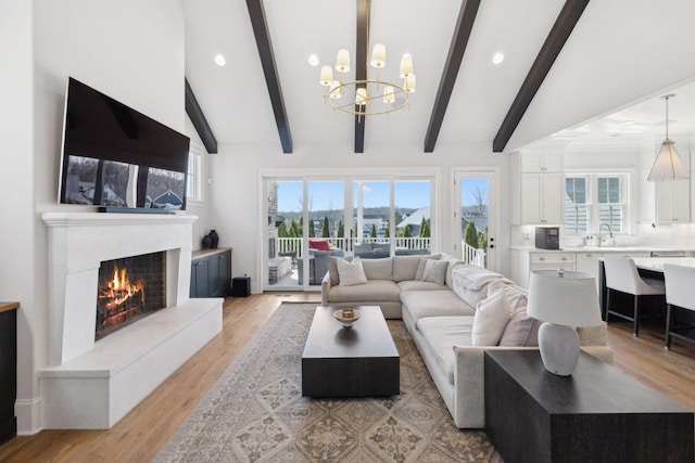 living area with high vaulted ceiling, a notable chandelier, a fireplace, beam ceiling, and light wood finished floors