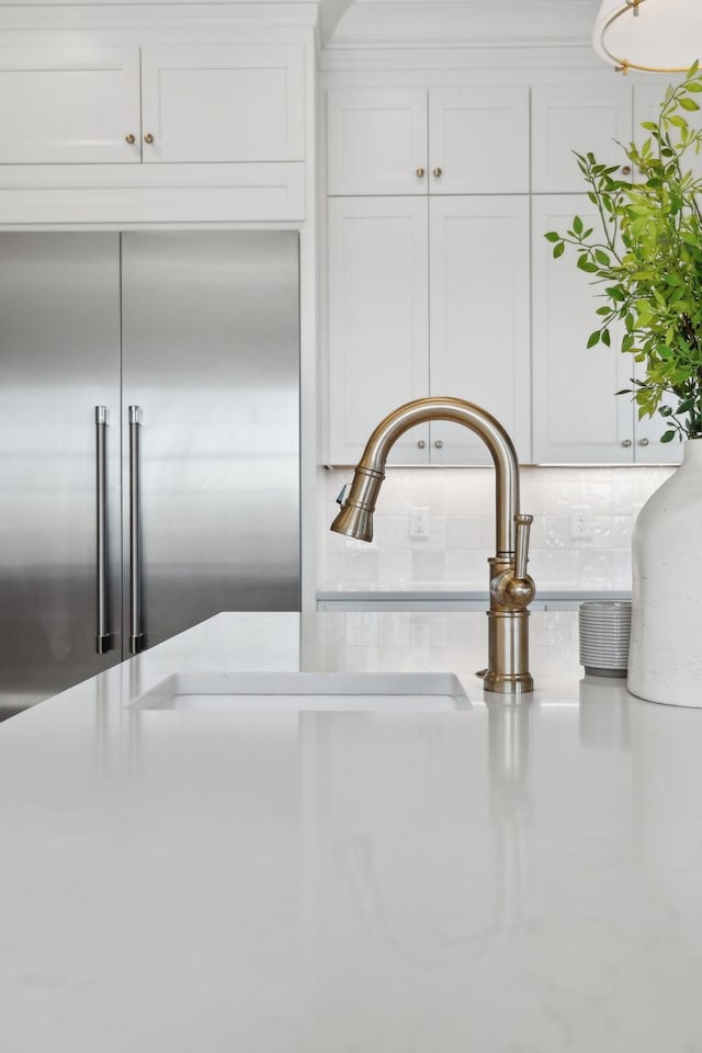 room details featuring white cabinets, decorative backsplash, light countertops, a sink, and built in fridge