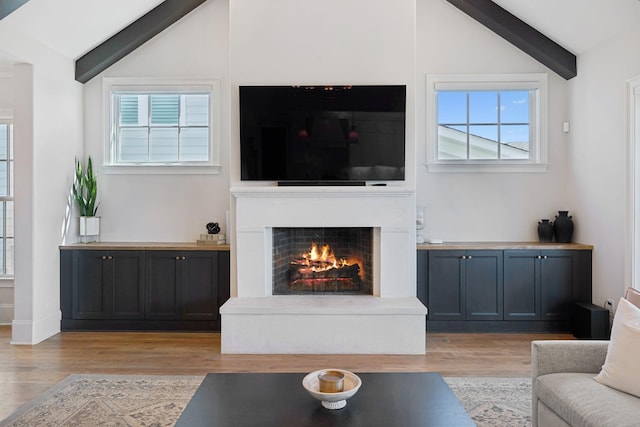 living area with plenty of natural light, vaulted ceiling with beams, and a lit fireplace