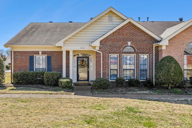 view of front of house featuring brick siding, roof with shingles, and a front yard