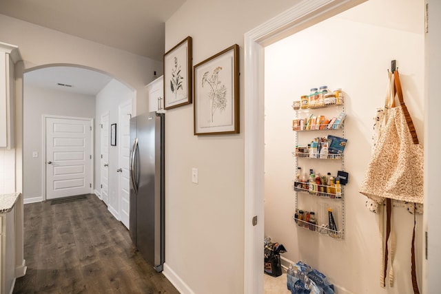 hallway featuring baseboards, arched walkways, and dark wood-type flooring