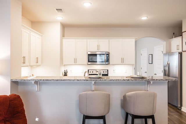 kitchen featuring stainless steel appliances, white cabinets, visible vents, and a kitchen bar