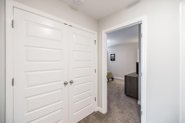 hallway with dark colored carpet and baseboards