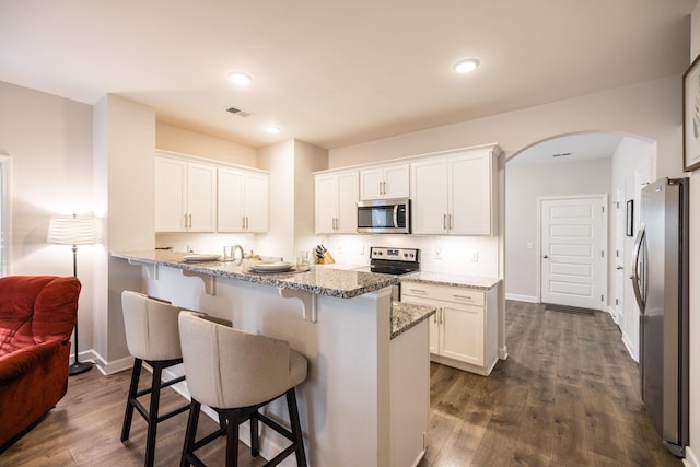 kitchen featuring white cabinets, appliances with stainless steel finishes, arched walkways, and a kitchen breakfast bar