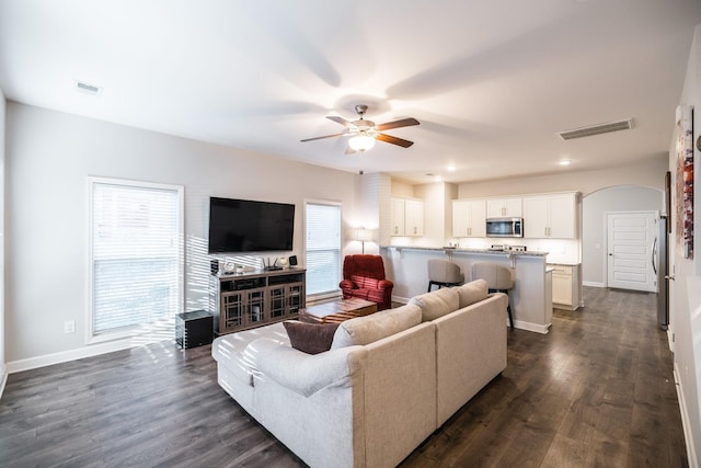 living area with arched walkways, visible vents, dark wood finished floors, and baseboards