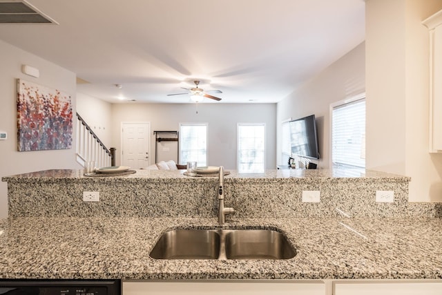 kitchen with light stone counters, a sink, a ceiling fan, open floor plan, and dishwasher