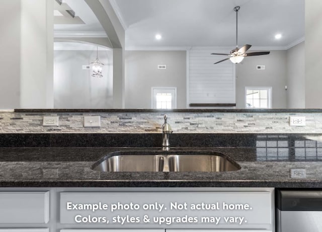 kitchen featuring crown molding, dark stone countertops, a sink, and stainless steel dishwasher