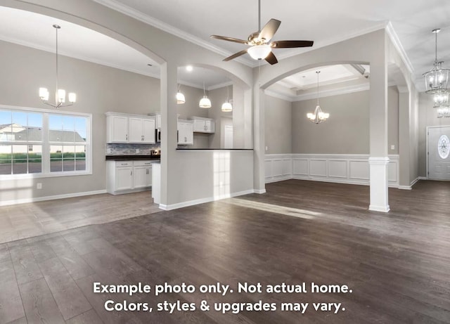unfurnished living room with dark wood-style floors, wainscoting, ornamental molding, and ceiling fan with notable chandelier