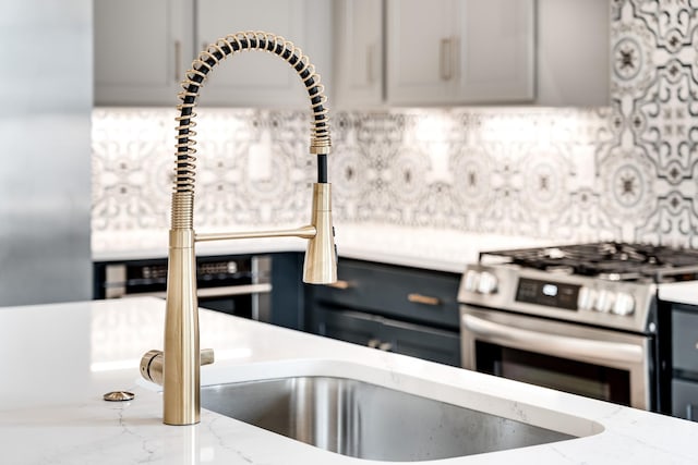 kitchen with tasteful backsplash, stainless steel gas range, light stone countertops, and gray cabinetry