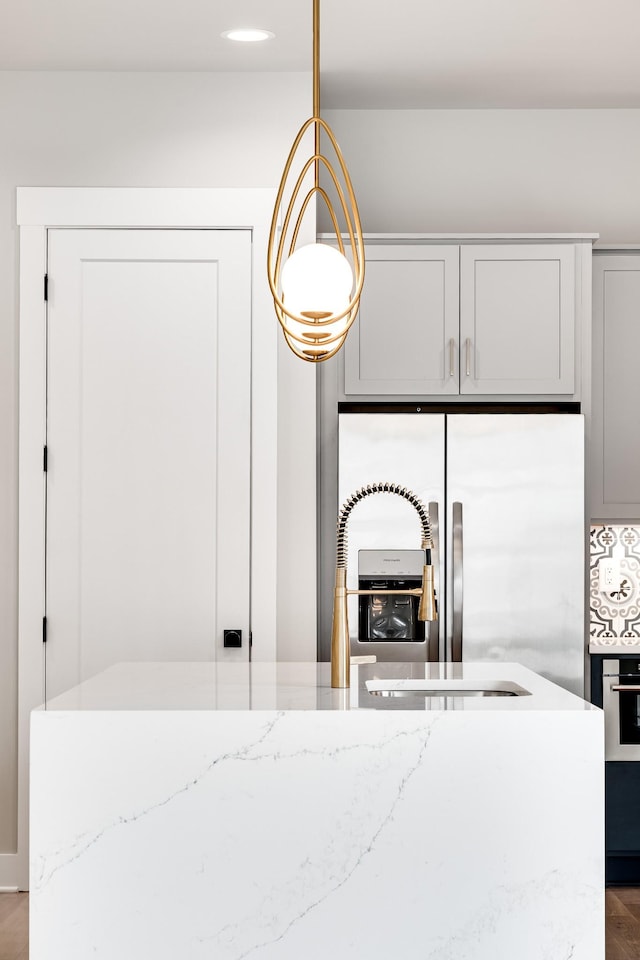 kitchen with stainless steel appliances, light stone counters, hanging light fixtures, and wood finished floors