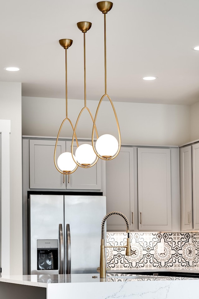 interior details with recessed lighting, stainless steel fridge, light stone counters, and gray cabinetry