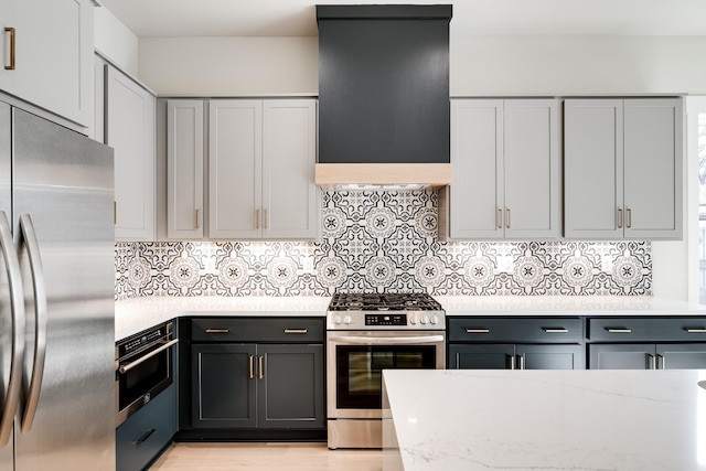 kitchen with light wood finished floors, tasteful backsplash, appliances with stainless steel finishes, light stone countertops, and exhaust hood