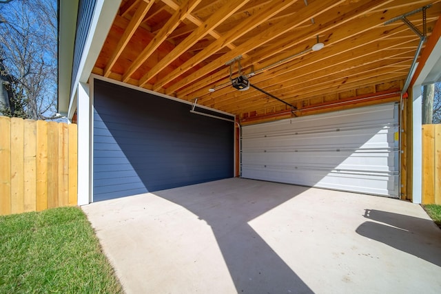 garage featuring concrete driveway, fence, and a garage door opener