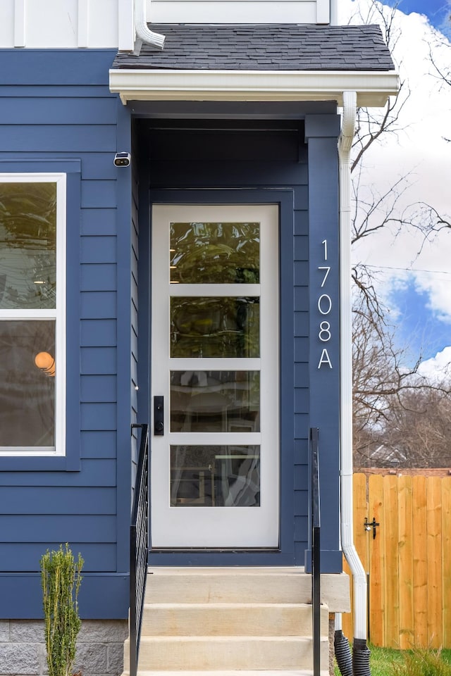 doorway to property with roof with shingles and fence