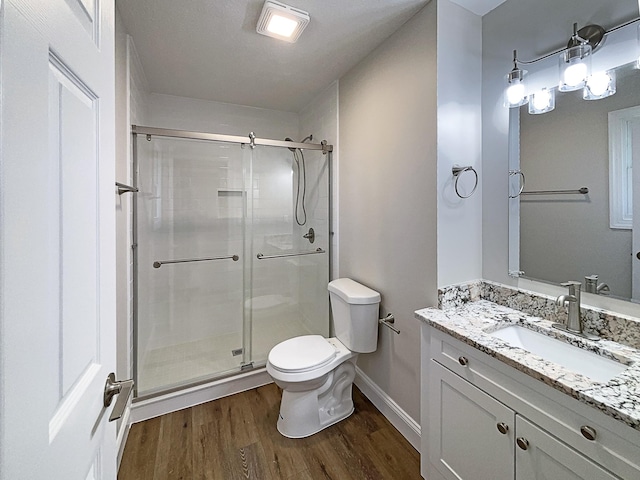 bathroom featuring baseboards, toilet, wood finished floors, vanity, and a shower stall