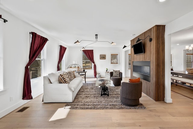 living room with a large fireplace, light wood-type flooring, visible vents, and an inviting chandelier