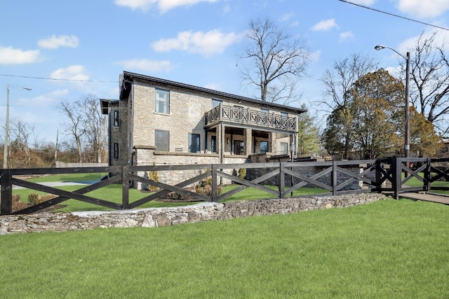 rear view of property with a yard, stone siding, and fence