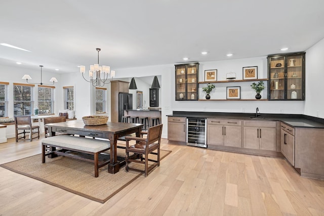 dining space featuring wine cooler, light wood-style flooring, recessed lighting, wet bar, and an inviting chandelier