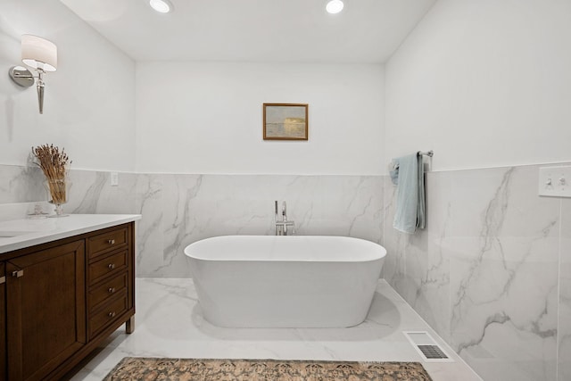 full bath with marble finish floor, recessed lighting, visible vents, a freestanding bath, and vanity