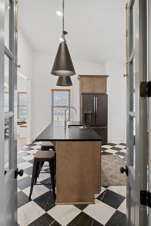 kitchen with dark countertops, stainless steel fridge, a sink, and a wealth of natural light