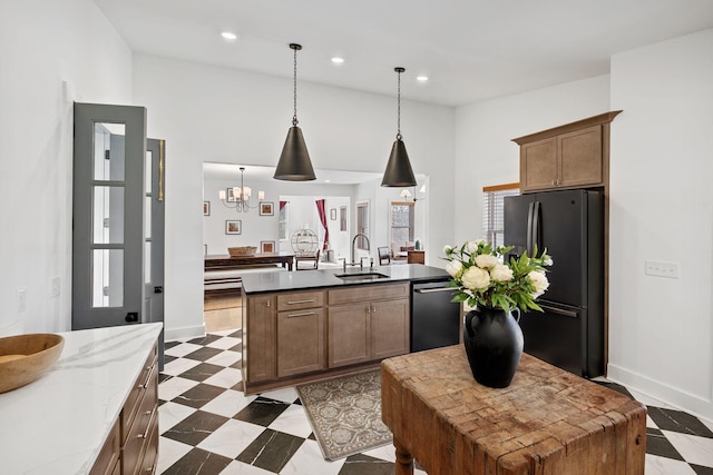 kitchen with dark floors, stainless steel dishwasher, freestanding refrigerator, a kitchen island with sink, and a sink