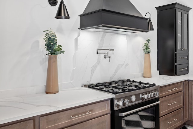 kitchen featuring light stone counters, premium range hood, backsplash, and stainless steel range with gas stovetop