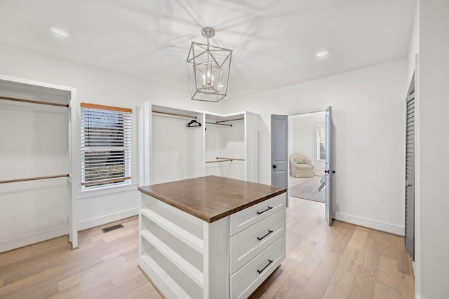 spacious closet with light wood-type flooring, visible vents, and an inviting chandelier