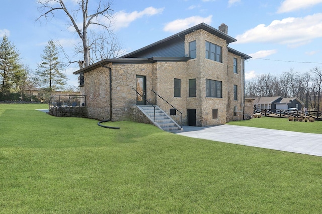 back of house with concrete driveway, a lawn, a chimney, and a patio