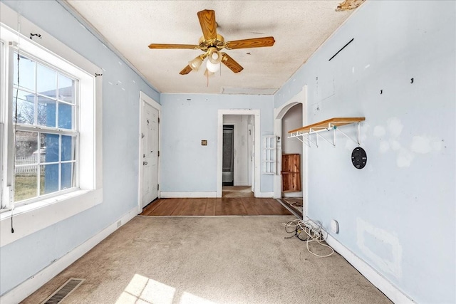 carpeted empty room featuring baseboards, visible vents, arched walkways, ceiling fan, and a textured ceiling