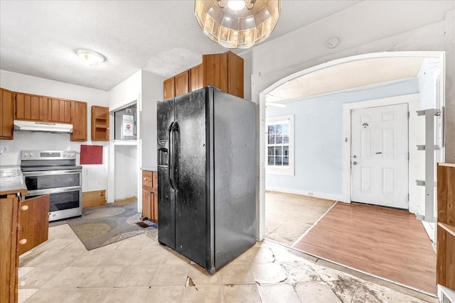 kitchen with range with two ovens, brown cabinets, under cabinet range hood, and black fridge