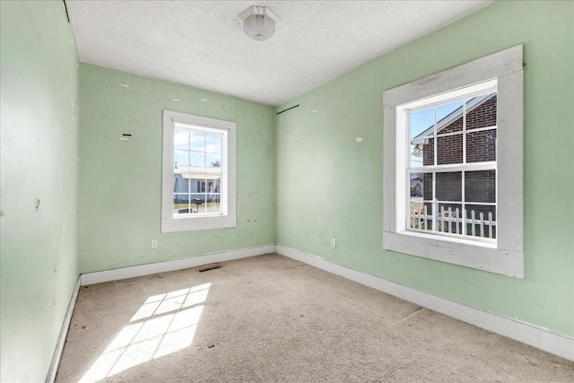 carpeted spare room featuring a textured ceiling, visible vents, and baseboards