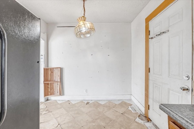 unfurnished dining area with a textured ceiling, light floors, and baseboards